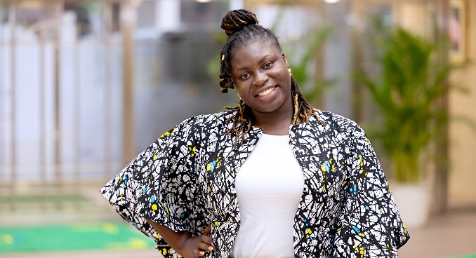 A young woman stands, smiling at the camera with her hand on her hip and head tilted to the side.