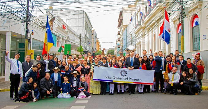 Un numeroso grupo de personas, algunas con banderas y una pancarta, posan para una foto en una calle.