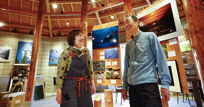 Dos personas sonríen una al lado de la otra sobre el fondo de una exposición fotográfica en un museo.
