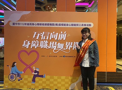 張晶惠站在一個橘色大海報前豎起大拇指拍照。