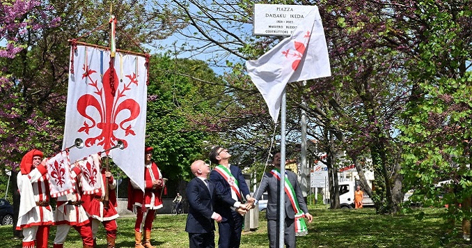 Three people unveiling a plaque and four bugle corps members with the flag of Florence.