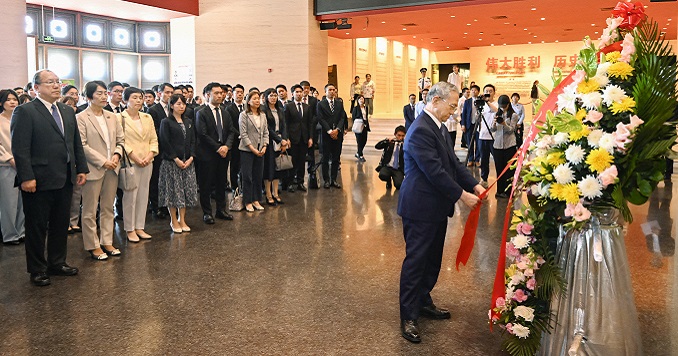 A group of people watch a man laying a wreath of flowers.