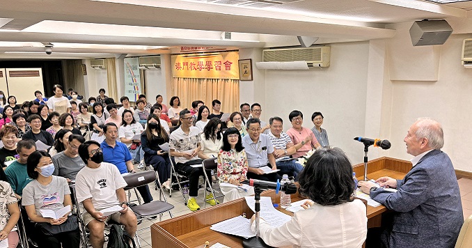 People seated in a room listening to two people on a stage.