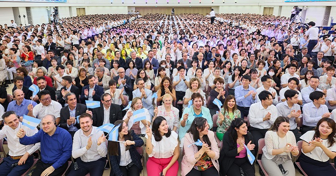 Hundreds of people gathered in a large hall, applauding.