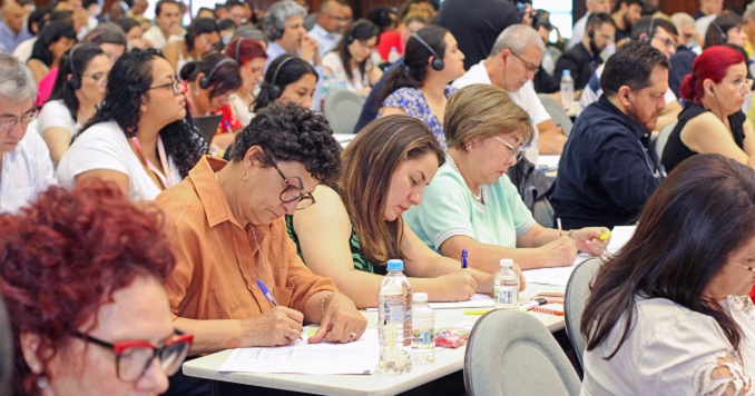 People seated in a hall writing notes during a lecture.