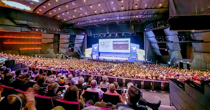 Personas sentadas en un gran auditorio mirando hacia el escenario donde tiene lugar una presentación durante una conferencia de diálogo interreligioso en Francia.