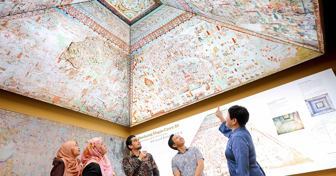 A group of five people looking up at a ceiling showing a reproduction of a historical cave art.