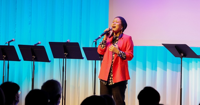 A lady in a red blazer sings into a microphone.