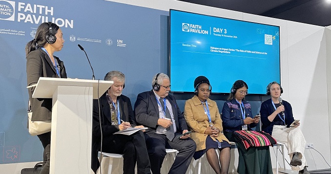 Un panel de seis personas sentadas en el escenario, con una de ellas de pie ante un atril, mientras que la panelista sentada a la derecha de la imagen habla por un micrófono.