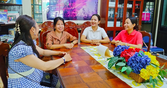 Four women seated around a table smiling at each other.