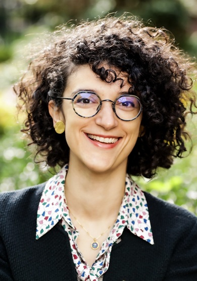 Woman with curly hair and glasses looking at the camera and smiling.