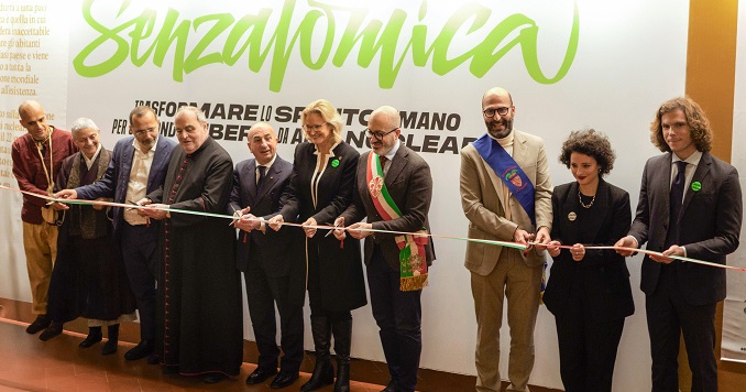 A group of people standing in a row behind a ceremonial ribbon, preparing to inaugurate an exhibition.