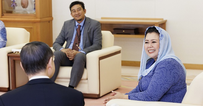 Woman with a head covering and two men in suits, sitting and smiling at a formal meeting. 