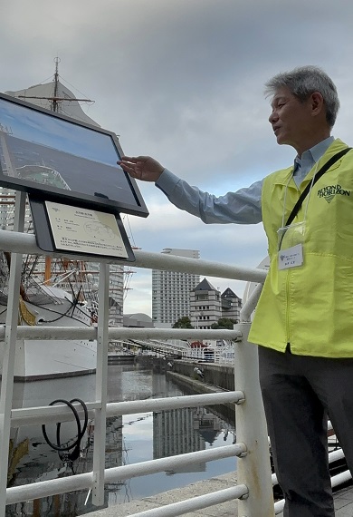 A man points to a photo of a ship on display outside.