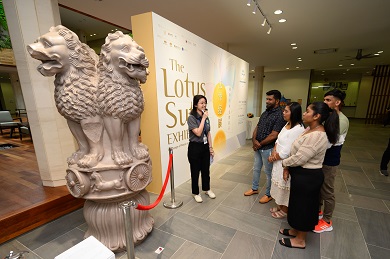People viewing a sandstone sculptural capital of four roaring lions, sitting on pedestal.