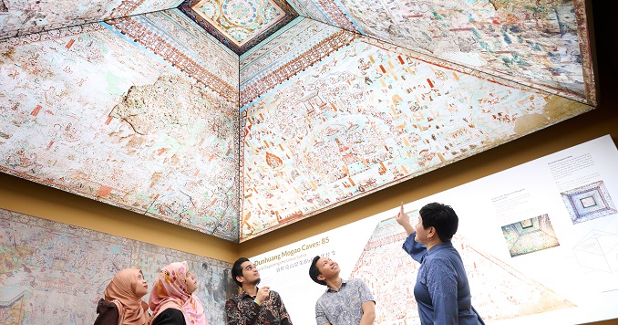 Five people viewing murals on the ceiling of a model of one of the Mogao caves