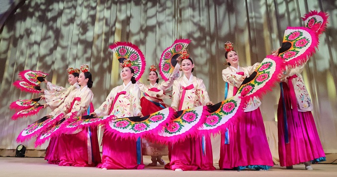 A group of performers in colorful dress doing a fan dance on stage.