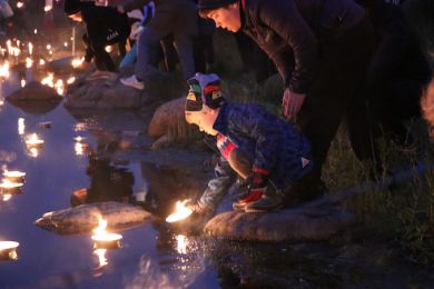 A woman and a child float a candle from the lake’s shore at night
